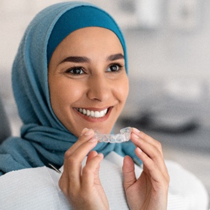 Woman in blue headwrap in dental chair holding Invisalign smiling