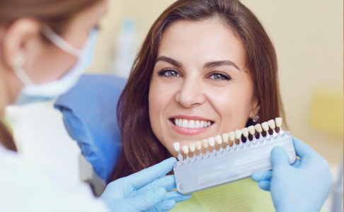 A dentist using a shade guide to assess a woman’s smile