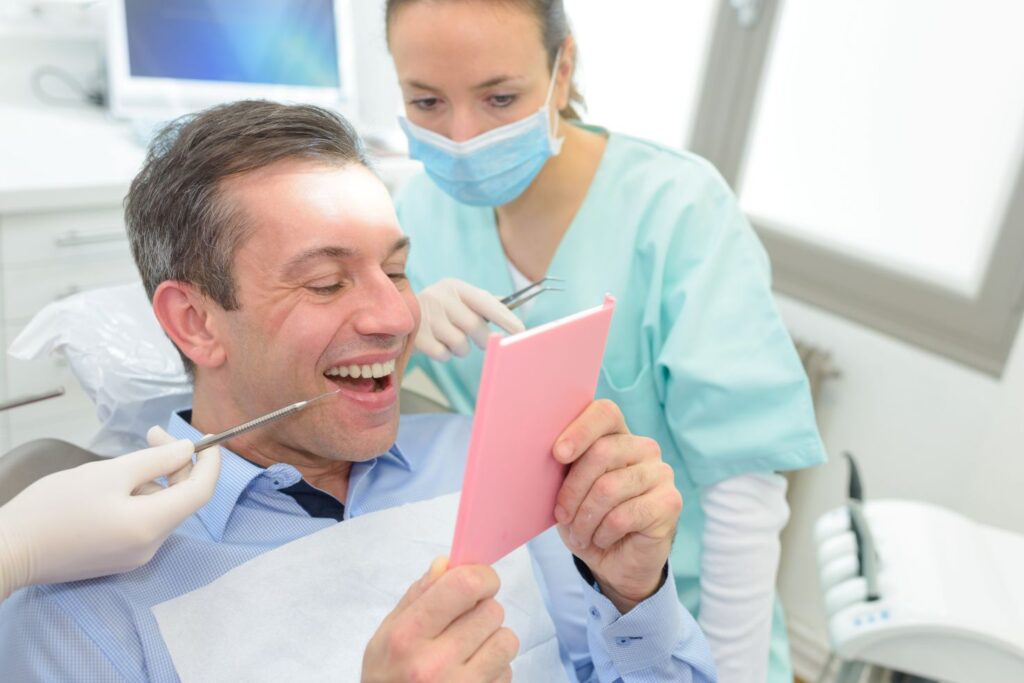 A man at the dentist’s office looking at his new dental crown in the mirror.